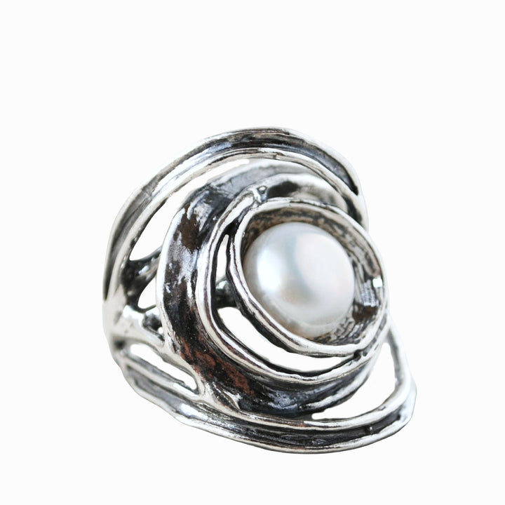 An artisan-crafted sterling silver ring with a freshwater pearl centered amidst swirling silver designs. Shown on a white background. 