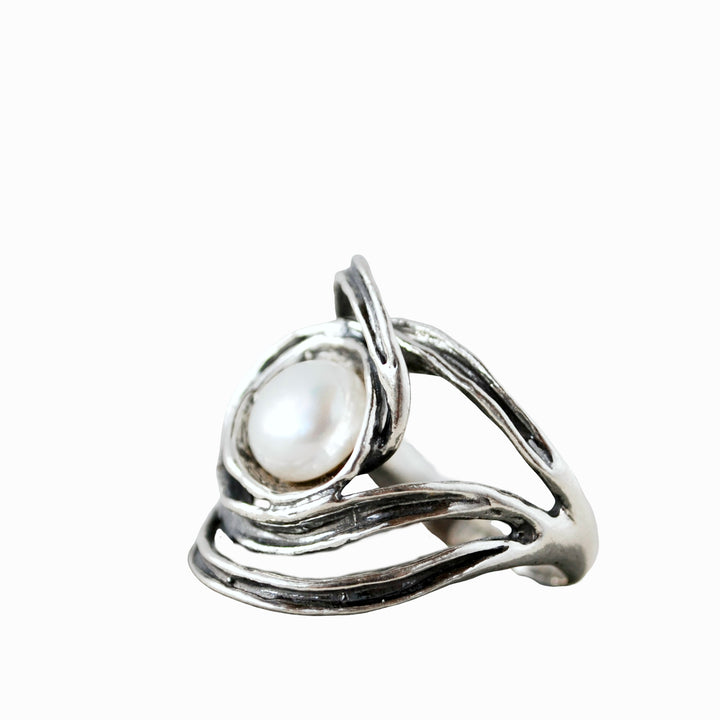 n artisan-crafted sterling silver ring with a freshwater pearl centered amidst swirling silver designs. Shown on a white background. 