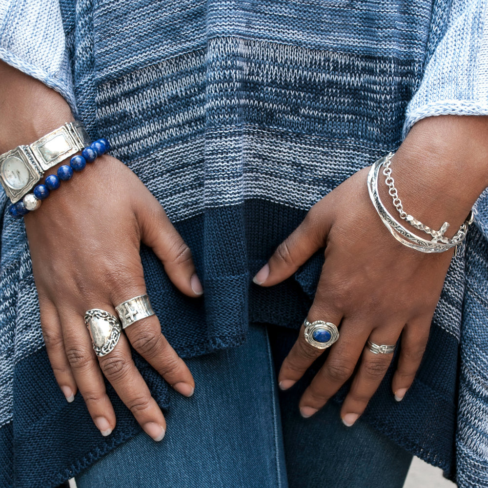 A silver band ring with a cross design is shown on a model. 