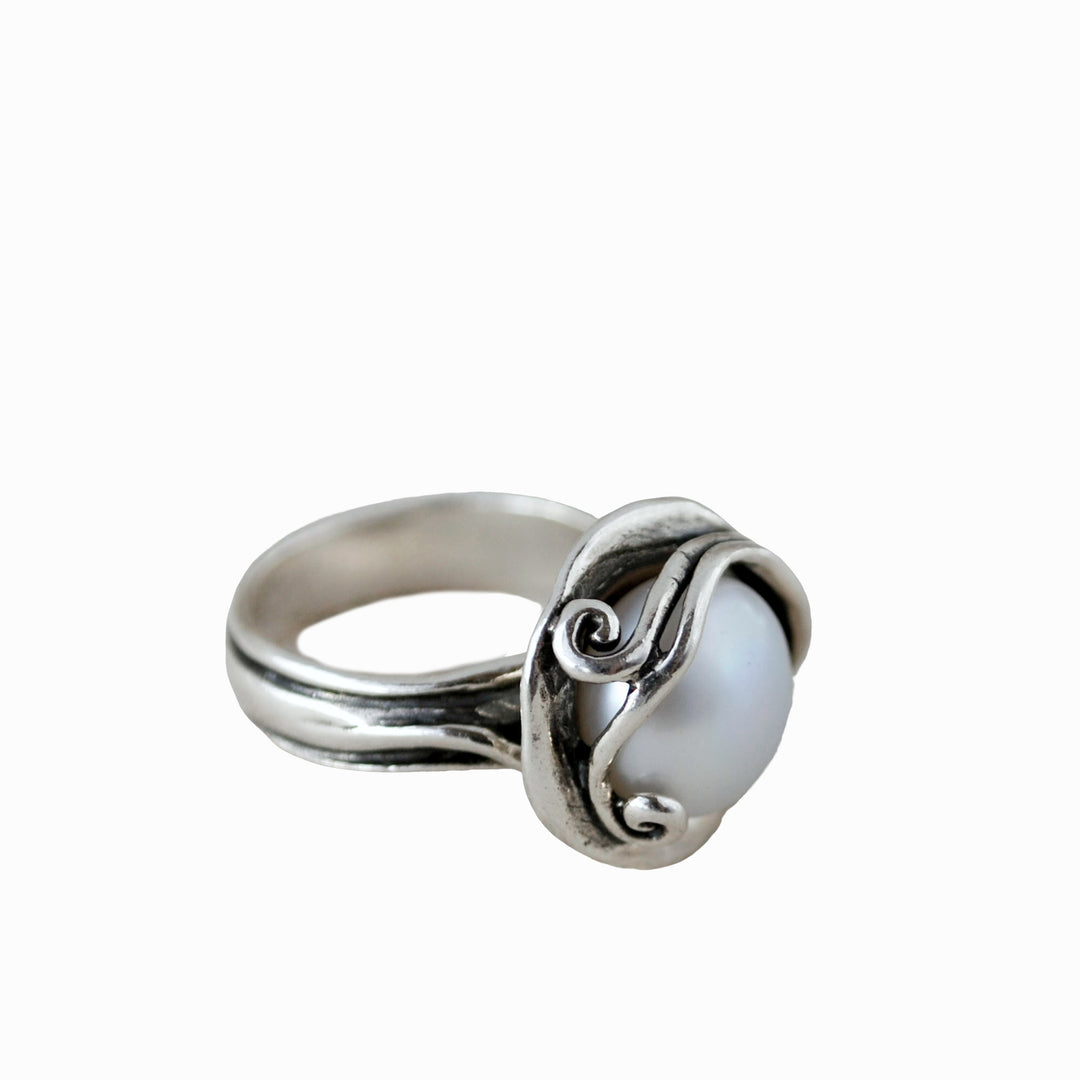 A sterling silver ring with a freshwater pearl nestled among sterling curls is shown from the side on a white background. 