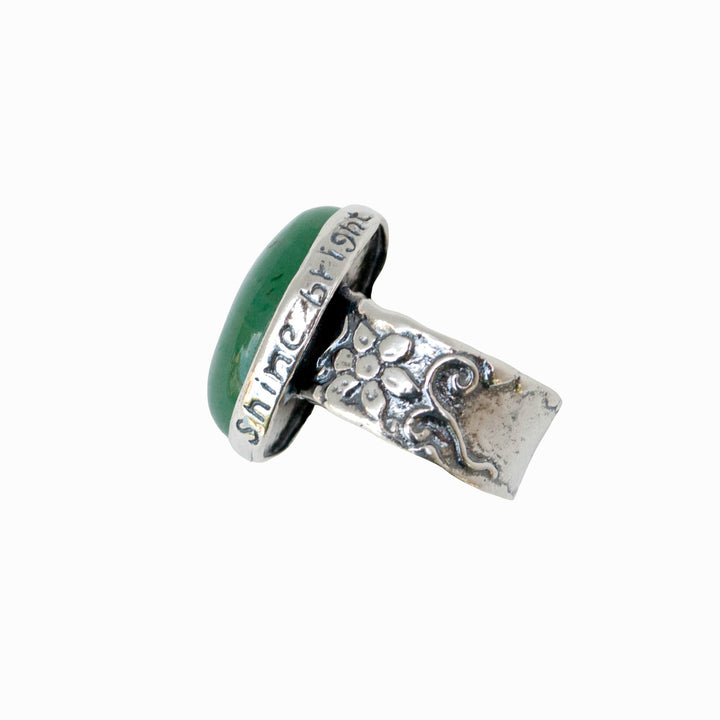 A sterling silver ring with a green adventurine stone set in a setting, featuring detailed work on the band. The words: shine bright are shown in this side view on a white background. 