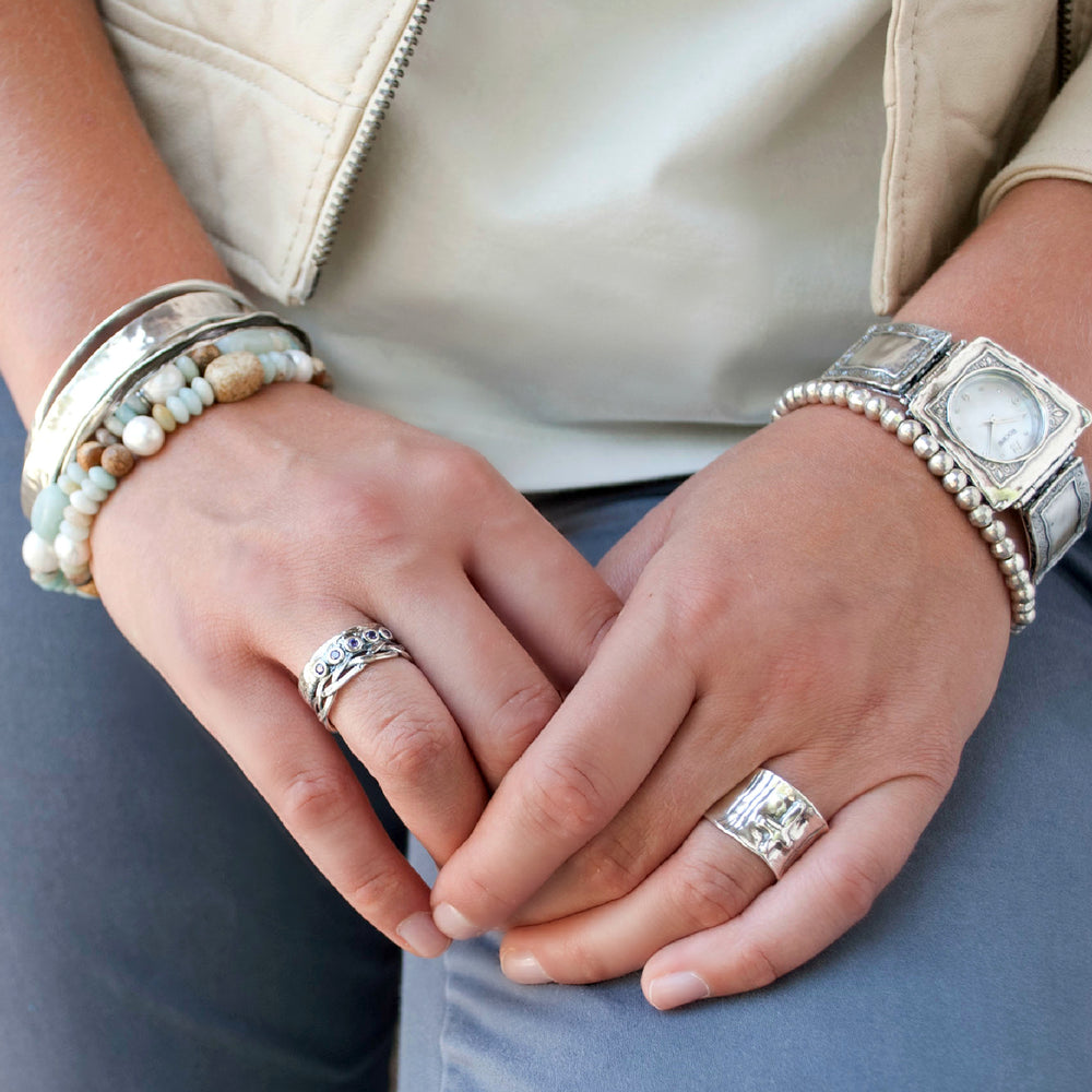 A sterling silver ring with a woven crown detail and bezel-set amethyst CZ stones. Shown on a model.