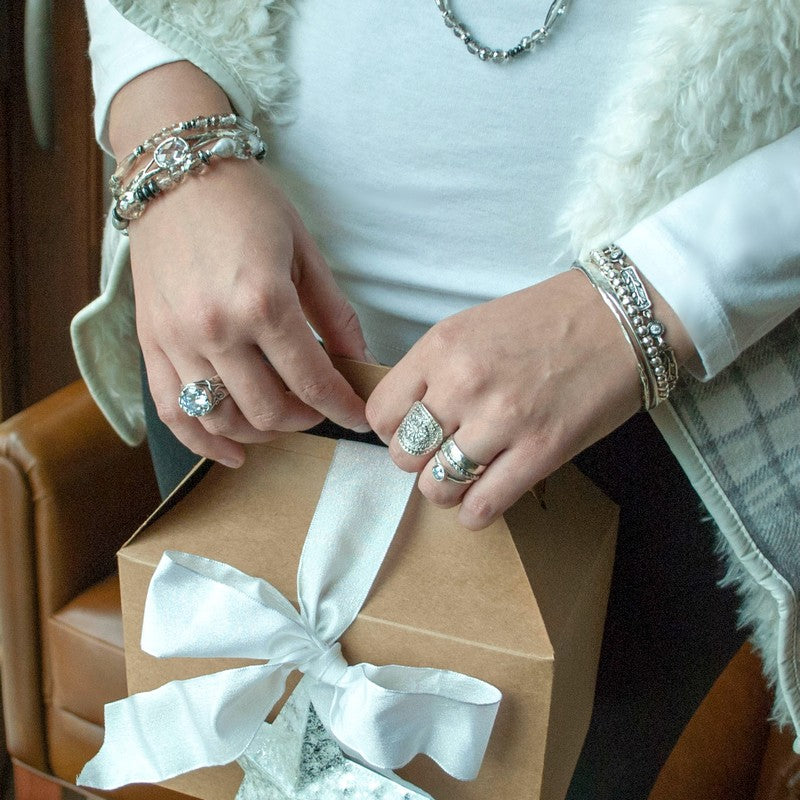 A set of three silver rings, with one central band featuring a clear cubic zirconia and two thinner bands onw with a textured band. Shown on a model.