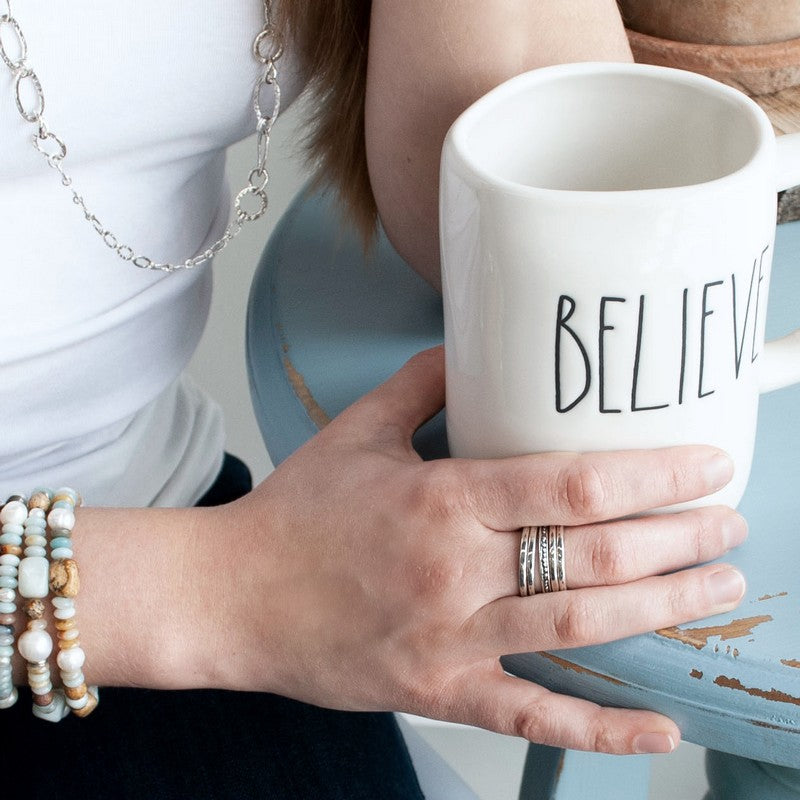 A set of five silver stackable rings with varying designs, four simple with one dotted, shown on a model.