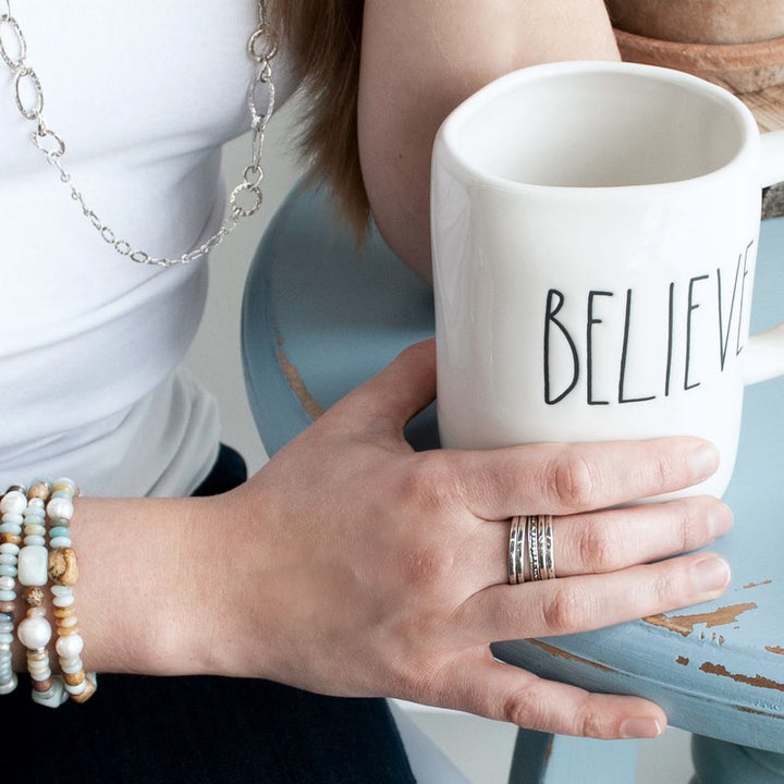 A set of five silver stackable rings with varying designs, four simple with one dotted, shown on a model.