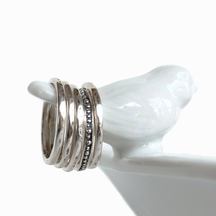 A set of five silver stackable rings with varying designs, four simple with one dotted, displayed on a white stand.