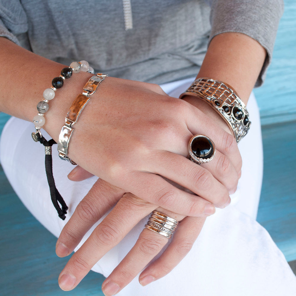 A ring with a gorgeous smooth cabochon of onyx,and a sparkling trio of CZs nestles in a unique setting. Shown on a model.