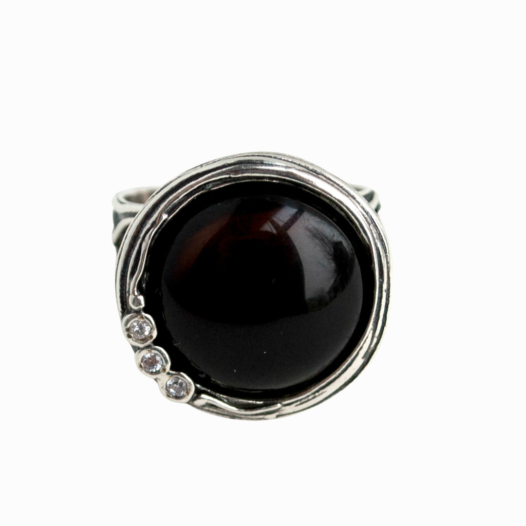 A ring with a gorgeous smooth cabochon of onyx,and a sparkling trio of CZs nestles in a unique setting. Front view shown on a white background.