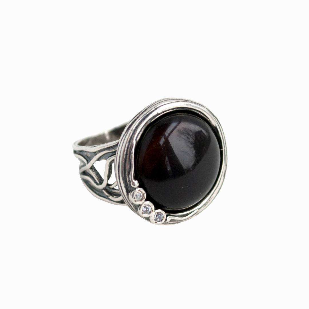 A ring with a gorgeous smooth cabochon of onyx,and a sparkling trio of CZs nestles in a unique setting. Shown on a white background.