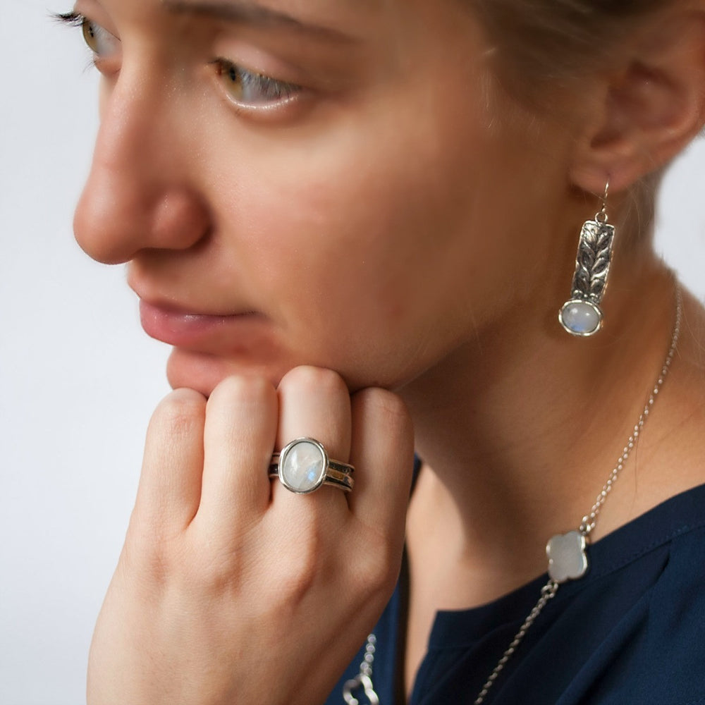 A pair of sterling silver earrings featuring rainbow moonstone cabochons and intricate leaf details, are shown on a model.