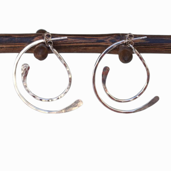 A pair of sterling silver hoop earrings with a hammered finish, displayed on a wooden dowel from the side. Showing its unique design. 