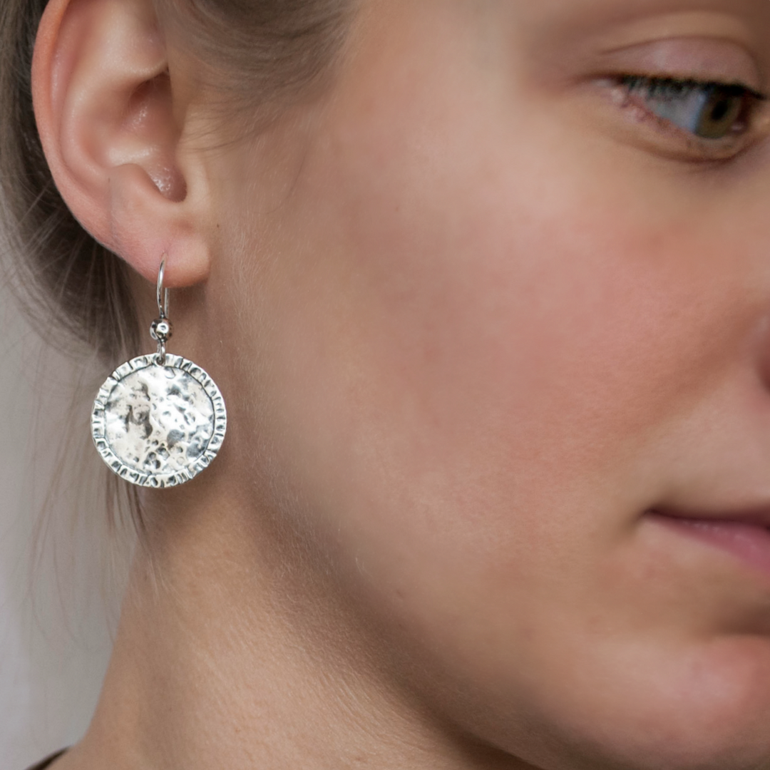 Round, dimpled sterling silver discs drop from French ear wires, are shown on a model. 