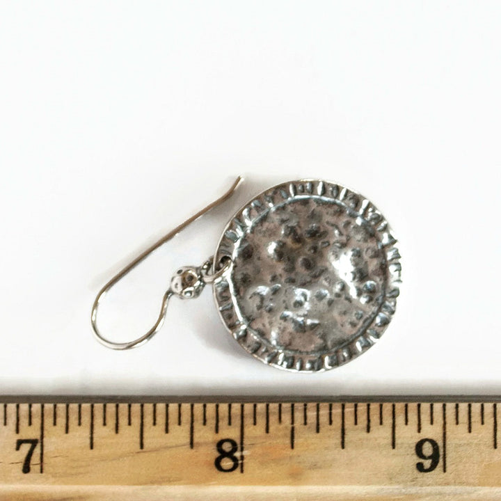 Round, dimpled sterling silver discs drop from French ear wires, displayed by a ruler for scale. 