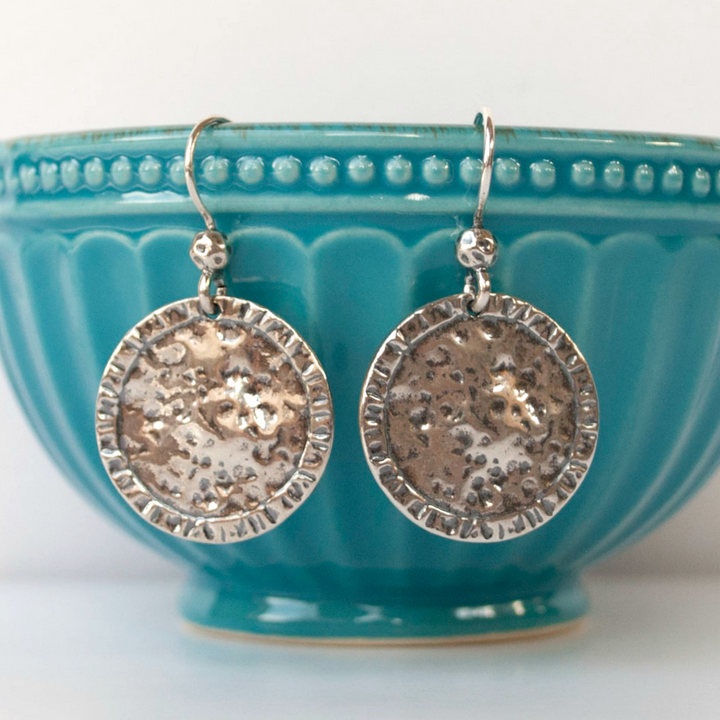 Round, dimpled sterling silver discs drop from French ear wires, displayed dangling on a turquoise bowl.