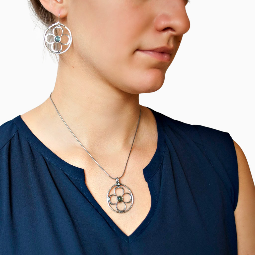 Round sterling silver earrings with a flower design and labradorite centers are shown on a model. Crafted of .925 sterling silver and cabachons of labradorite