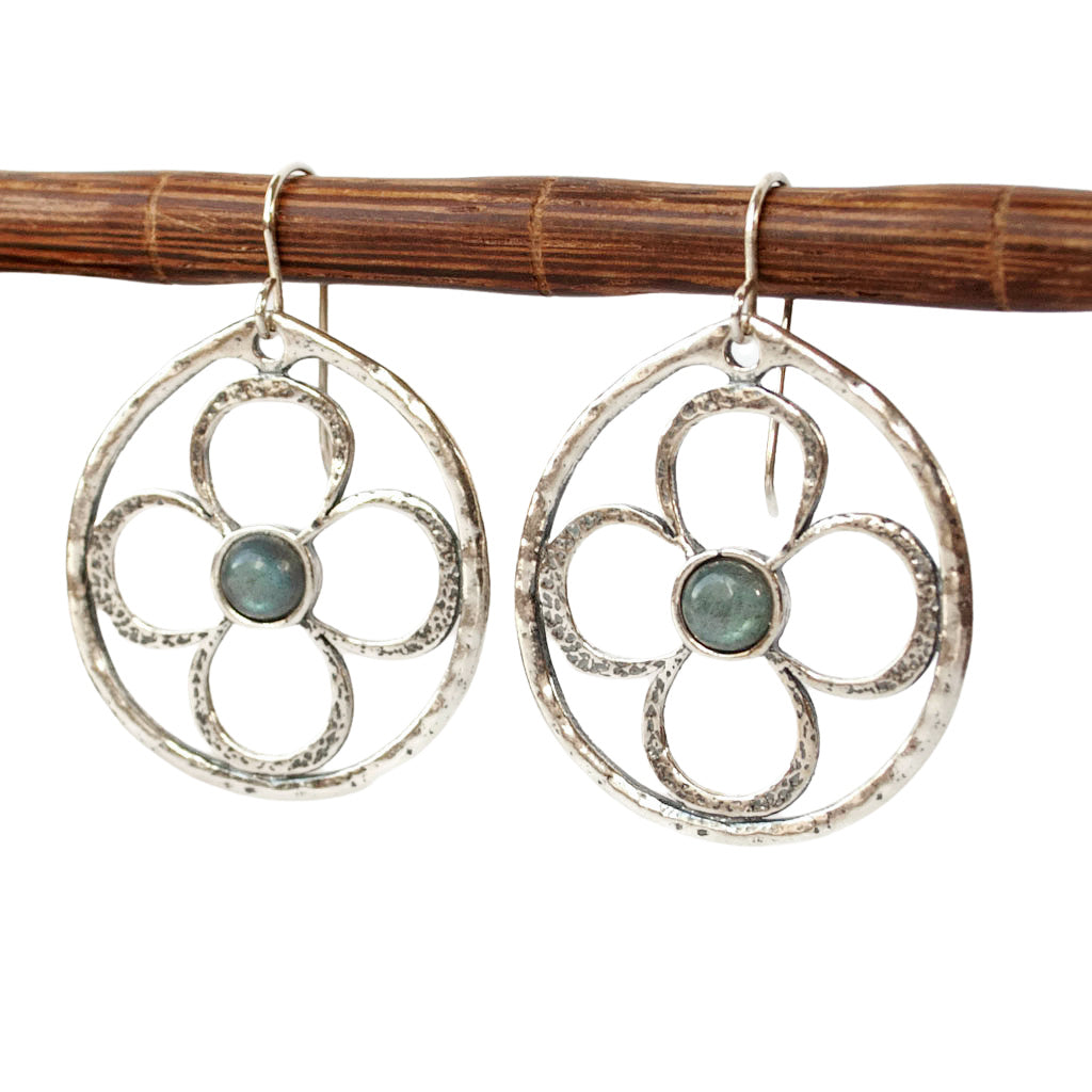 Silver earrings with a flower design and labradorite centers are shown from the front, dangling from a wooden dowel.