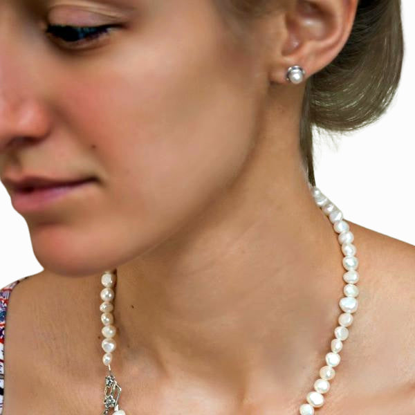 A pair of sterling silver post earrings featuring white freshwater pearls is shown on a model. 