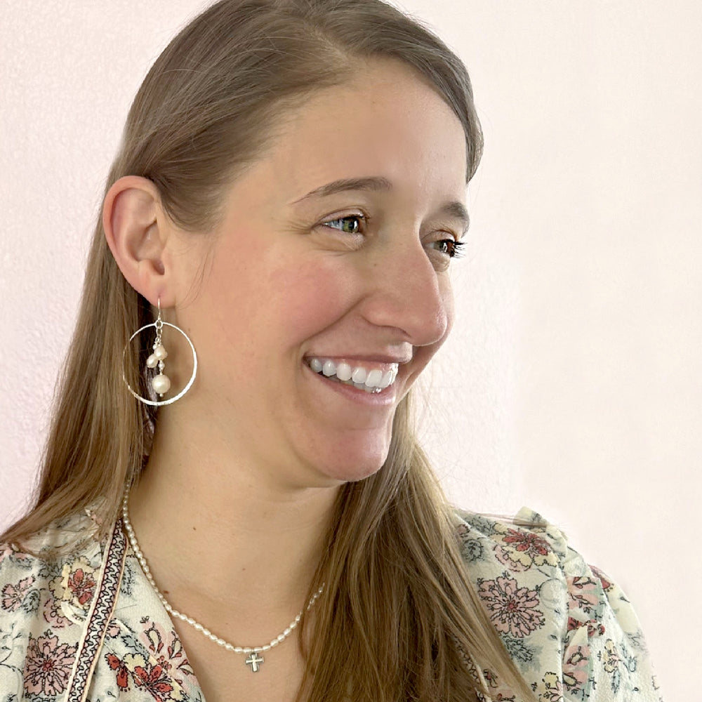 A pair of sterling silver hoop earrings with freshwater pearls dangling in the center. Shown on a model.