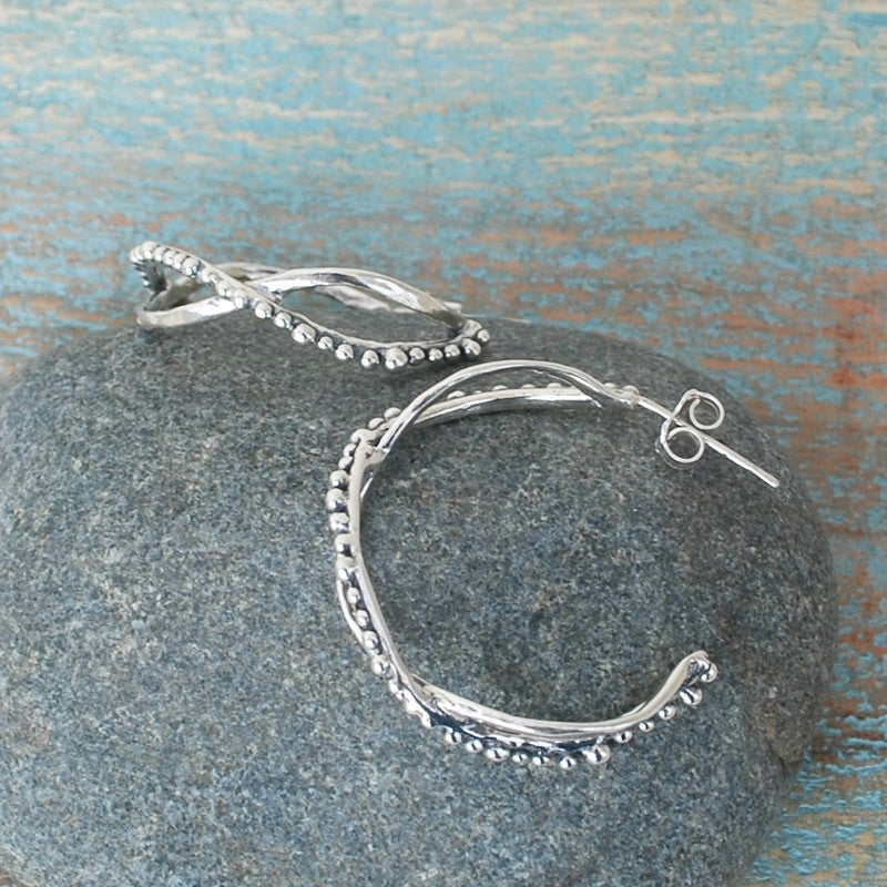 Sterling silver double-hoop earrings feature two distinct hoops, one adorned with tiny beads. Shown on a grey rock with side view displayed. 