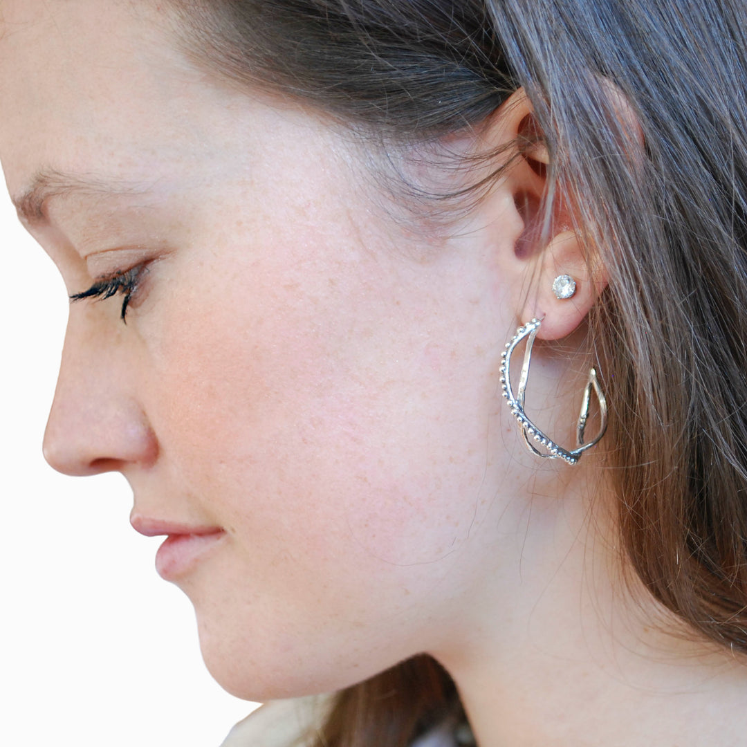 A close-up image of a woman's ear wearing a silver hoop earring with tiny beads connected to a larger hoop.