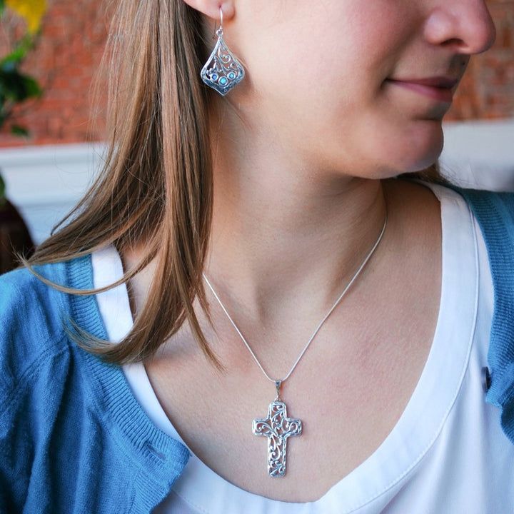Trio of lab created blue opal is bezel set in each sterling silver earring. They are artisancrafted with scroll details. Dangle from a French ear wire. Shown on a model with our silver scroll cross necklace.