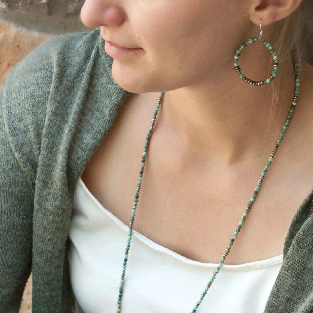 A pair of turquoise and hematite stone beaded hoop earrings with sterling silver French ear wires, shown on a model. 