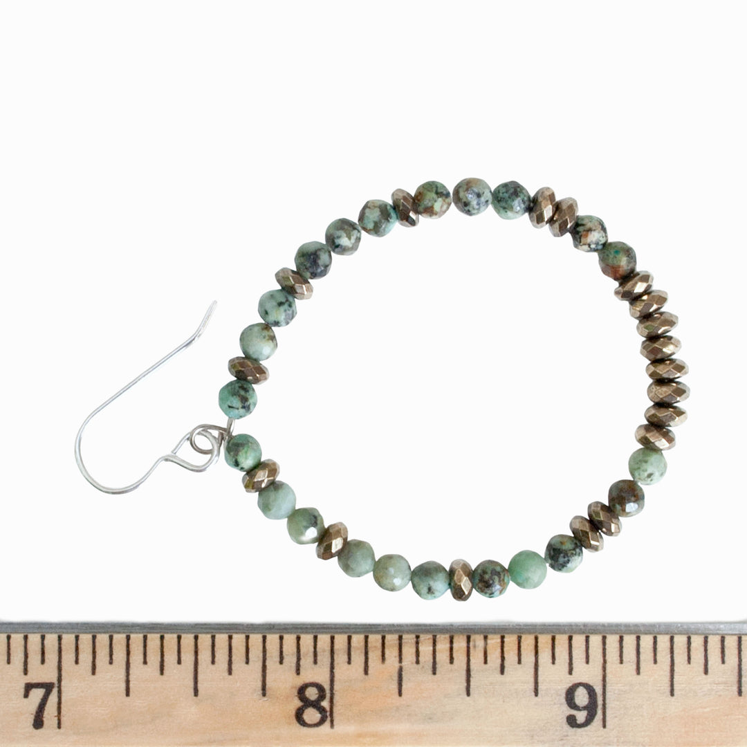 A pair of turquoise and hematite stone beaded hoop earrings with sterling silver French ear wires, displayed by a ruler on a white background to show scale. 