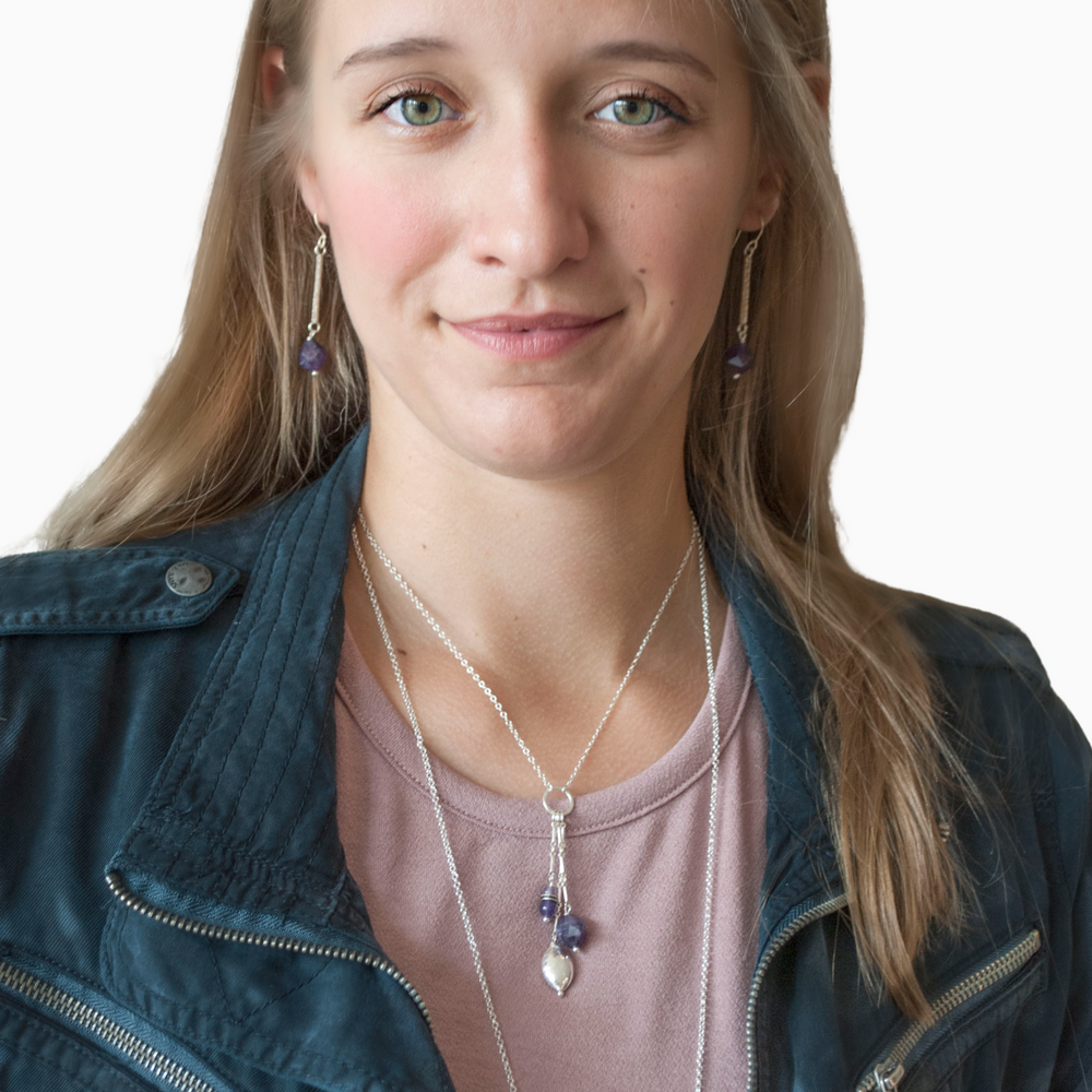 A pair of cut amethyst beads dangle from hammered sterling silver bars. Shown on a model. 