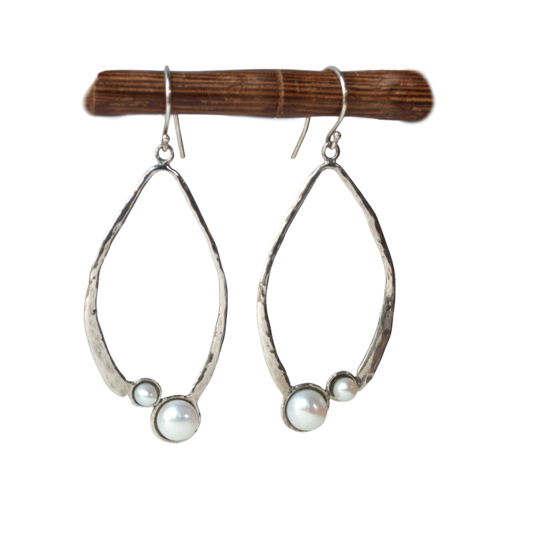 A pair of sterling silver hoop earrings with freshwater pearls attached to them, displayed on a wooden stick.