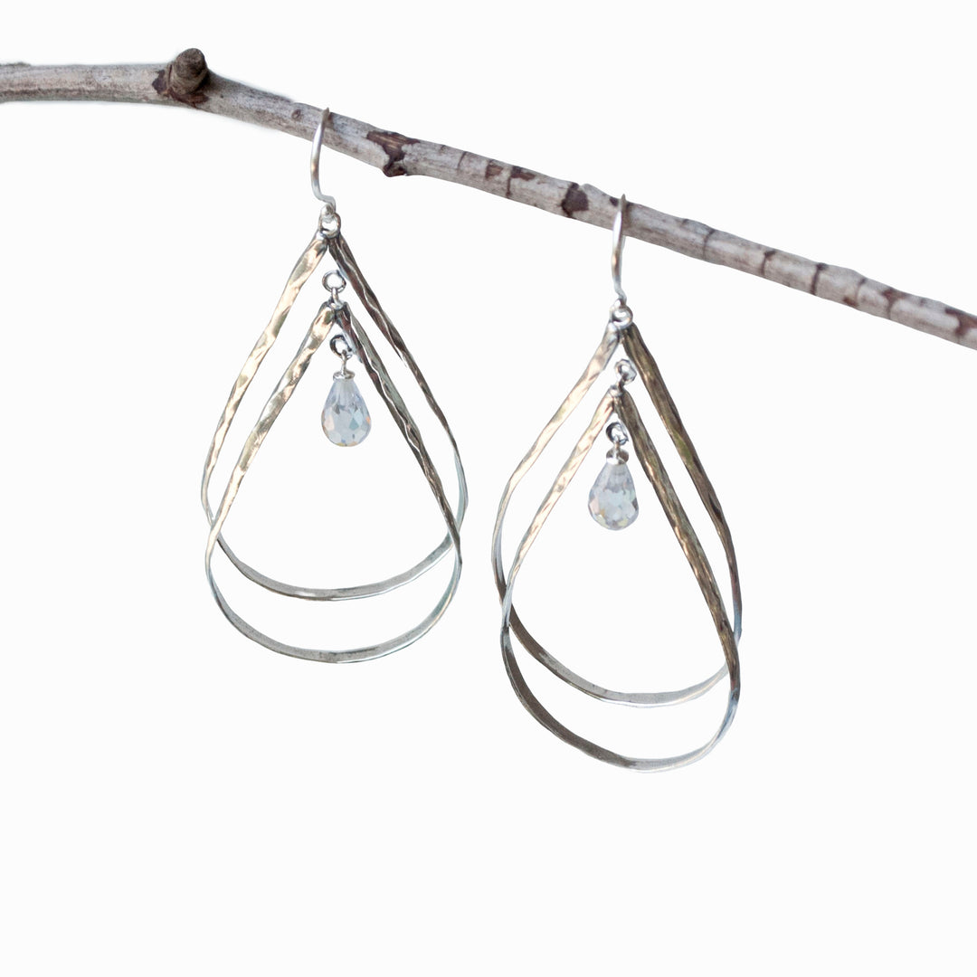 Silver Dangle Earrings- Large with double sterling silver tear-shaped drops. Features a dainty faceted clear CZ within. Shown dangling from a branch on a white background. 