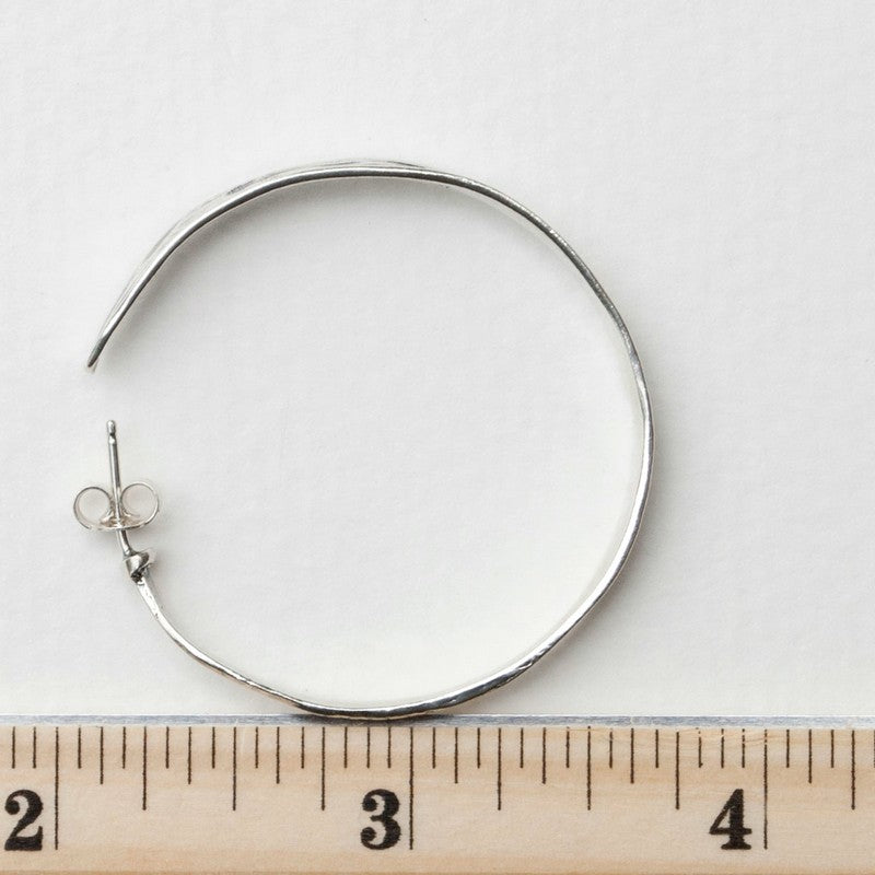 Sterling silver textured hoop earrings shown from the side with a ruler for size.
